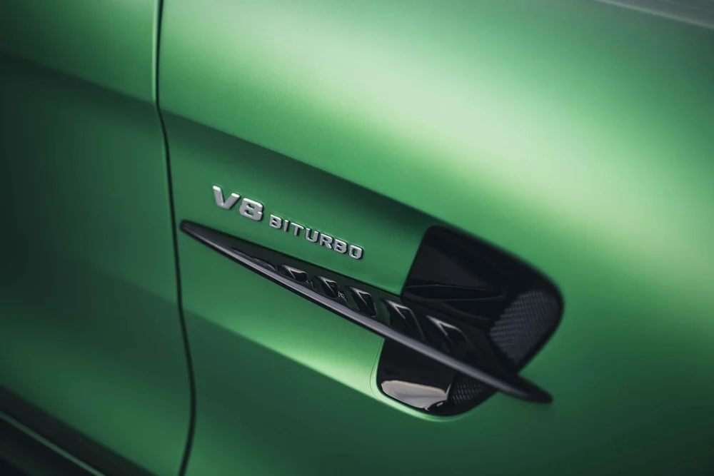 Silver V8 BITURBO lettering above a black fender vent on the softly lit green side panel.