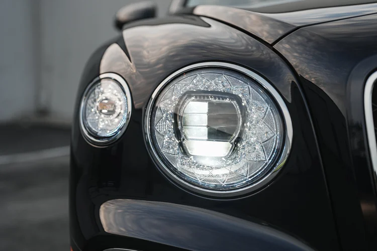 Illuminated circular headlamp framed by reflections in the dark front fender.