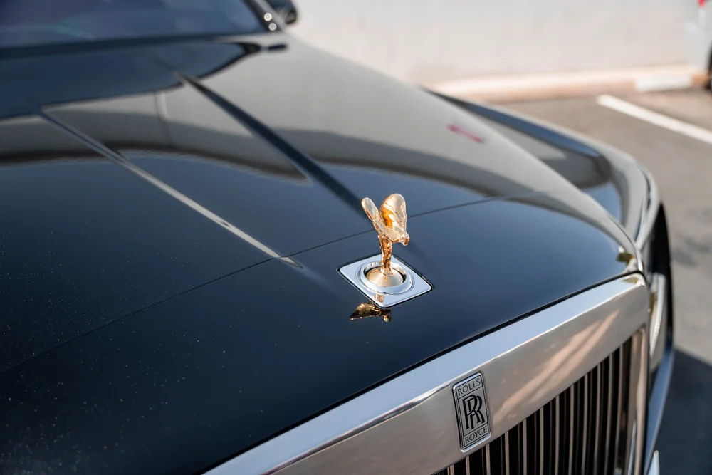Black Rolls-Royce Cullinan with Chrome Exterior Trim — gold-colored hood ornament and bright upper grille in a landscape detail