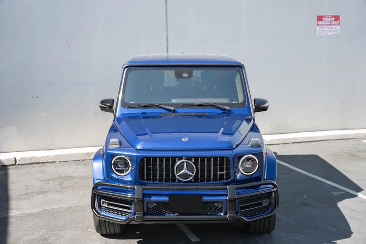 Complete high straight front view of the blue G 63 showing its hood contours, circular lamps, dark grille and front tires