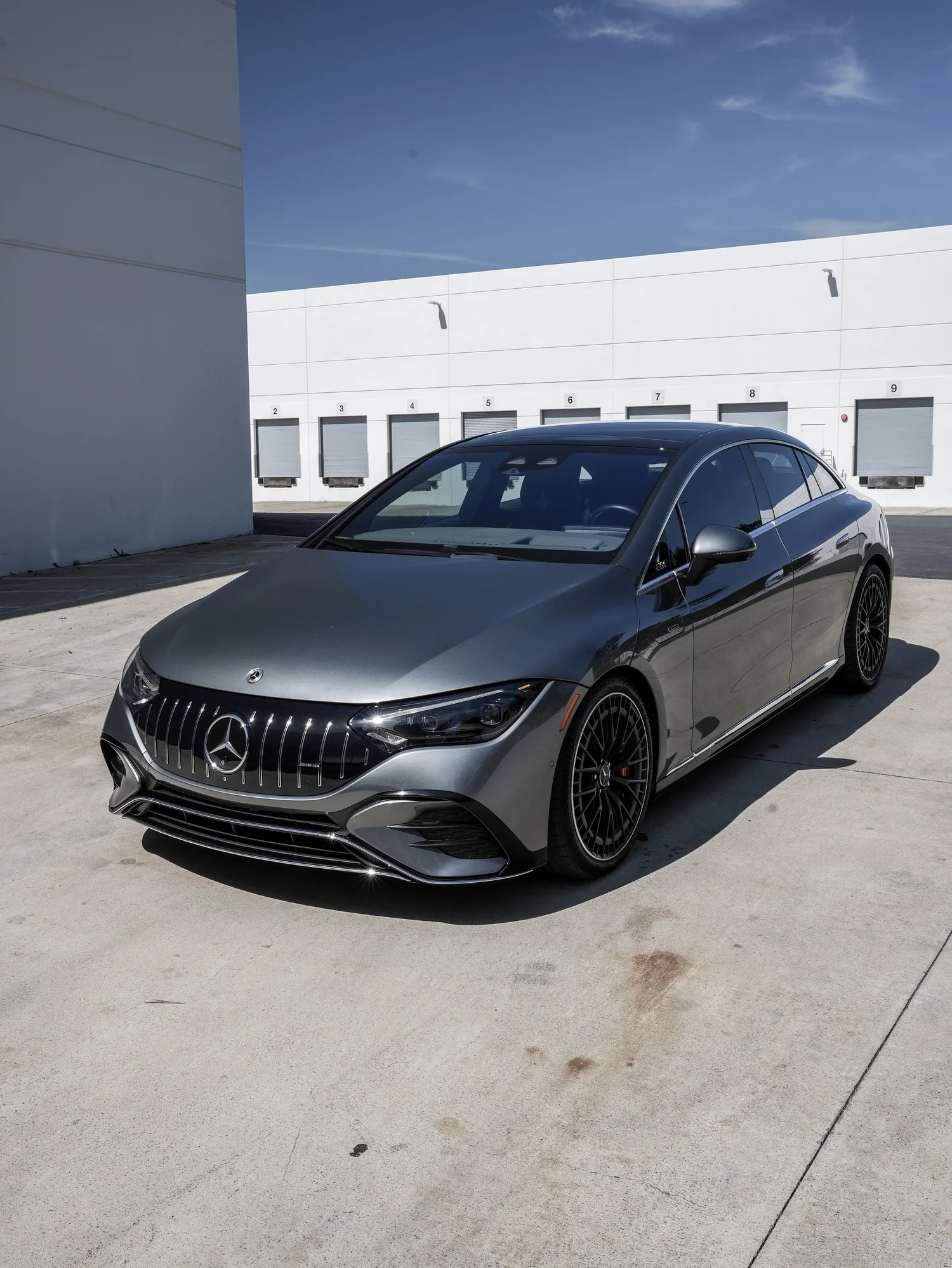 Front three-quarter view of the gray Mercedes-AMG EQE 53 with black multi-spoke wheels outside white workshop doors.
