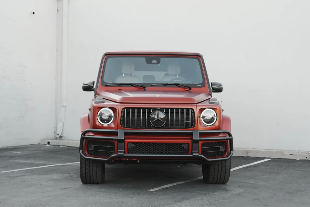 Centered full front view of the red G63 with both round headlights, vertical grille and black bumper guard