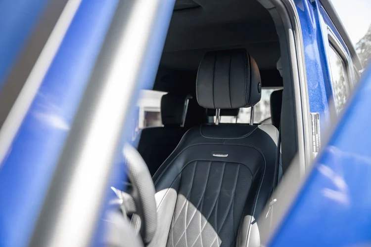 Dark perforated seat and headrest with vertical stitching and a small AMG plaque viewed through the blue G 63 door opening