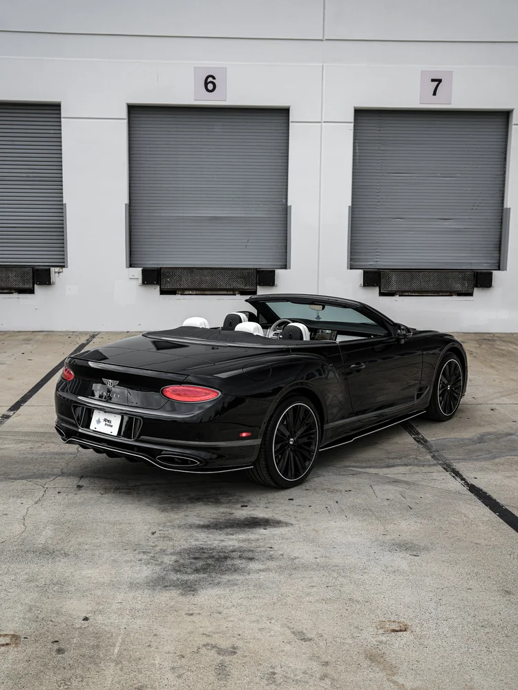 Onyx Black Bentley Continental GTC in rear three-quarter view with its open cabin, black wheels and oval taillamps.