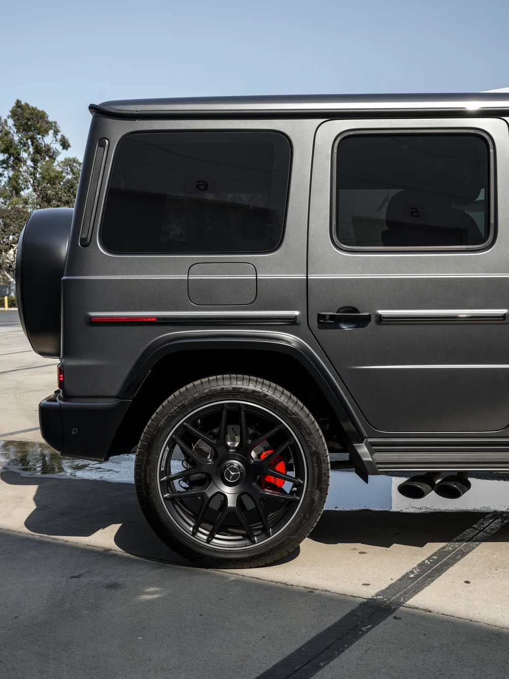 Rear side profile of the satin grey Mercedes-AMG G 63 showing dark windows, fuel flap, black wheel and twin side exhaust