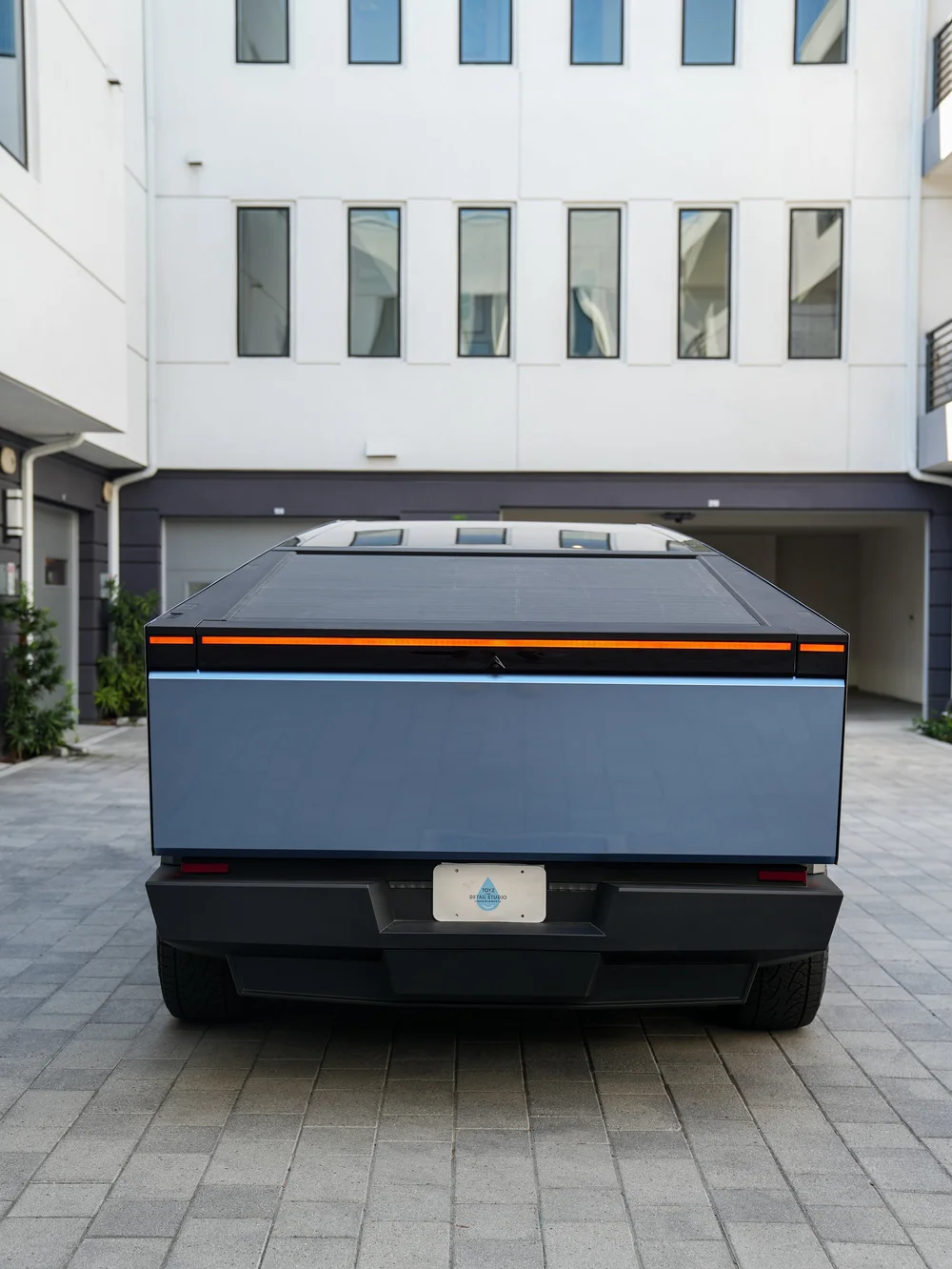 Straight rear view of the blue-gray Cybertruck with its broad tailgate, closed gray bed cover, illuminated rear lamp strip and black bumper.