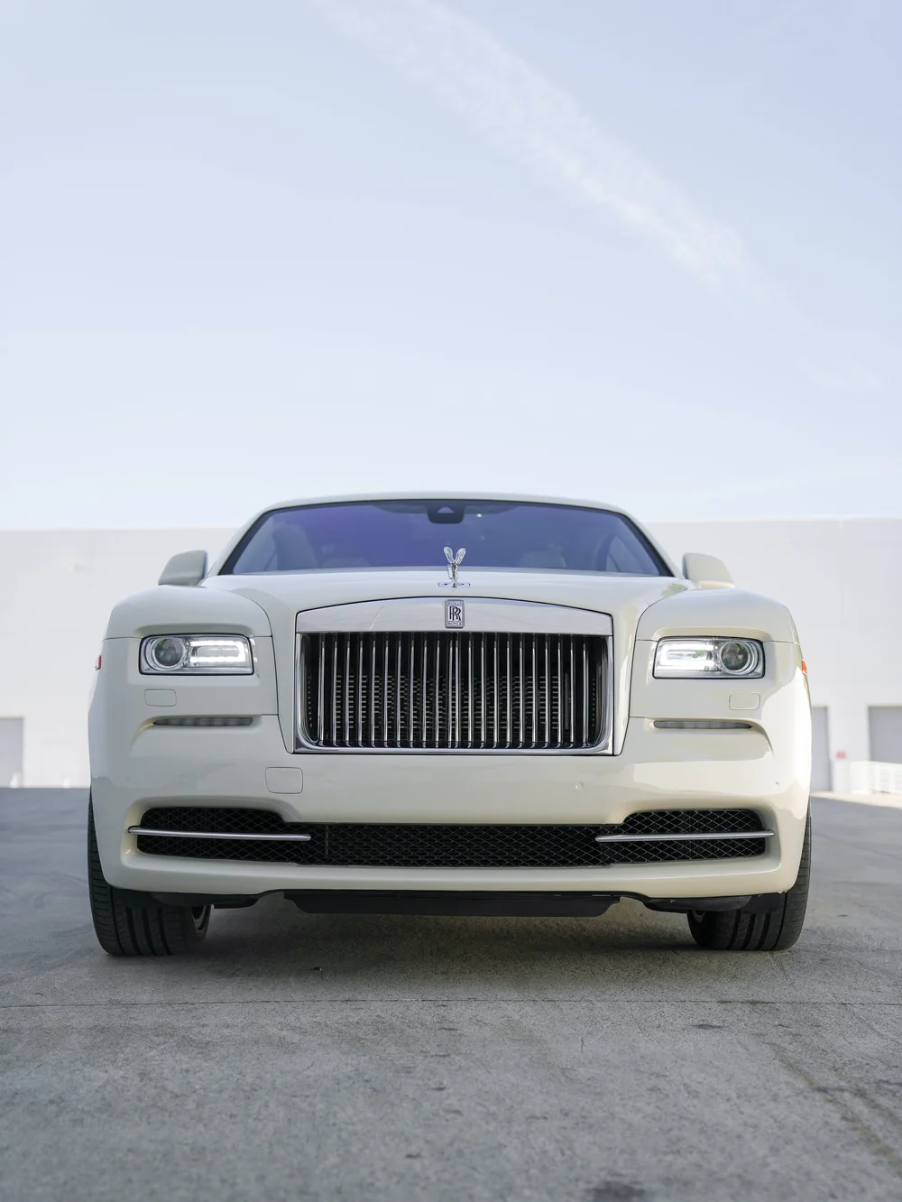 Low straight-front view of the pale Rolls-Royce Wraith with both headlights, grille and front tires.