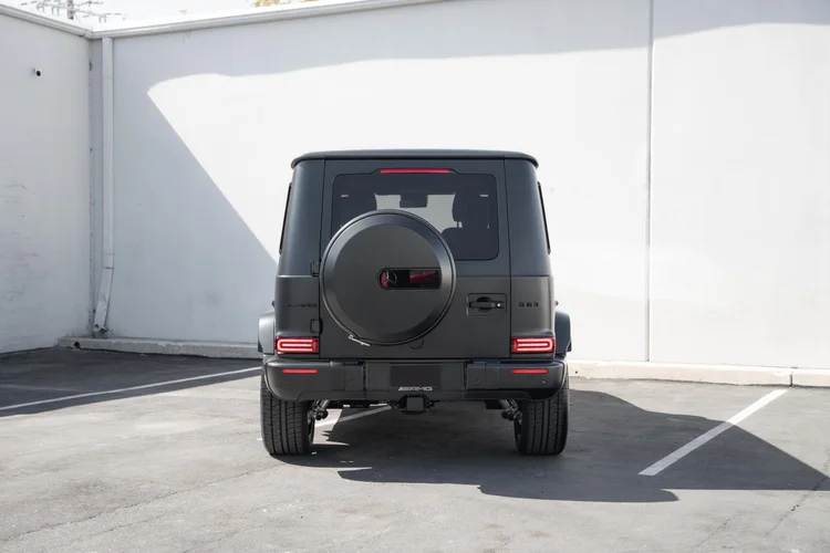 Complete straight rear view of the grey G 63 with red lamps and a round spare-wheel cover against a white wall