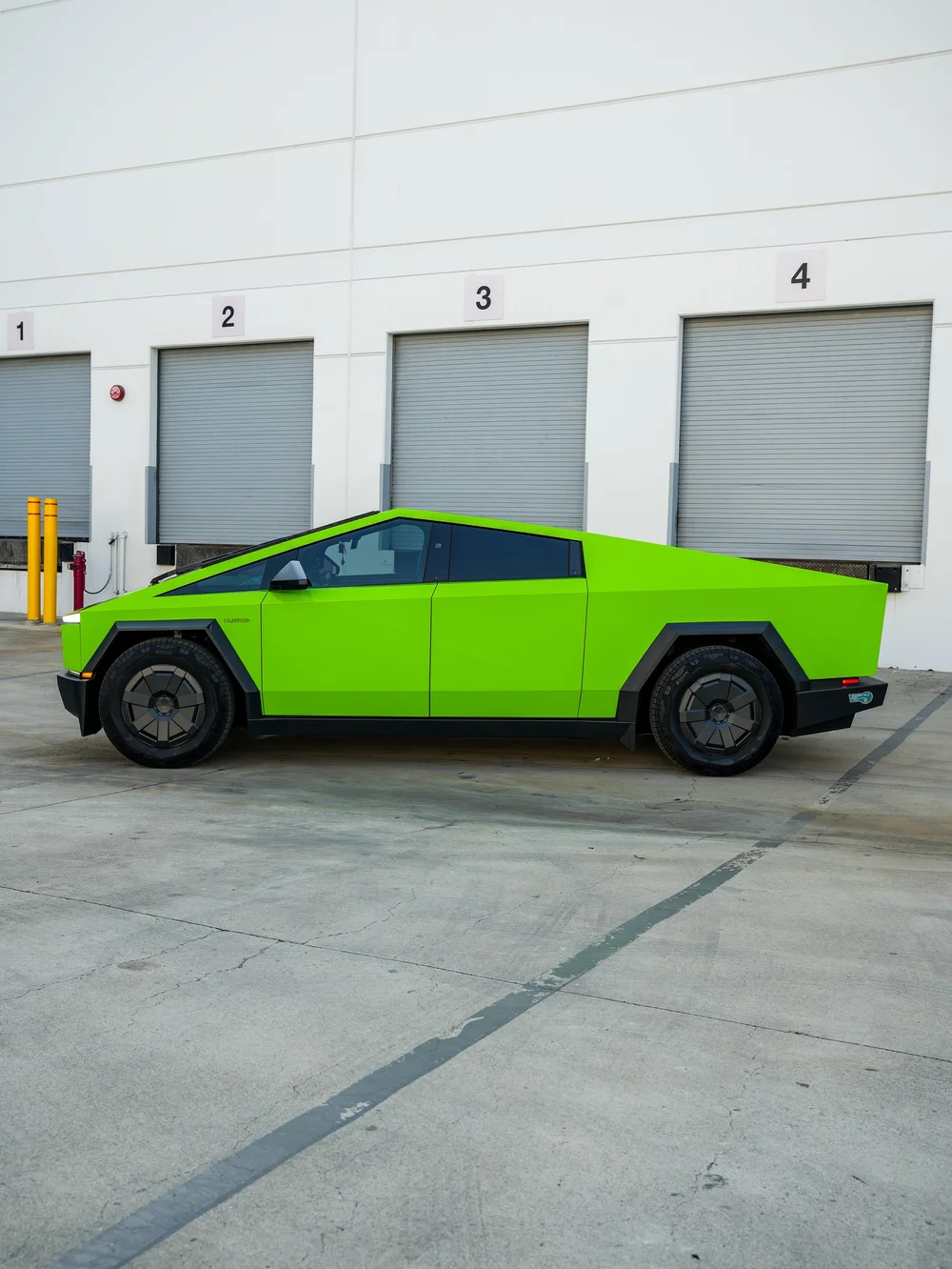 Complete side profile of the green Cybertruck showing its triangular roofline, straight green doors and rear side panel above two dark wheels.