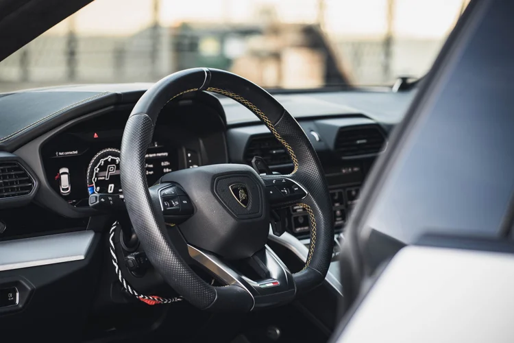 Lamborghini steering wheel and illuminated instrument display inside the dark cabin, framed by the open door.