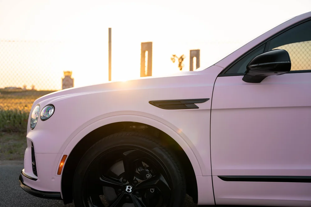 Bentayga pink front fender and door with a black side vent, mirror and wheel in low sunlight
