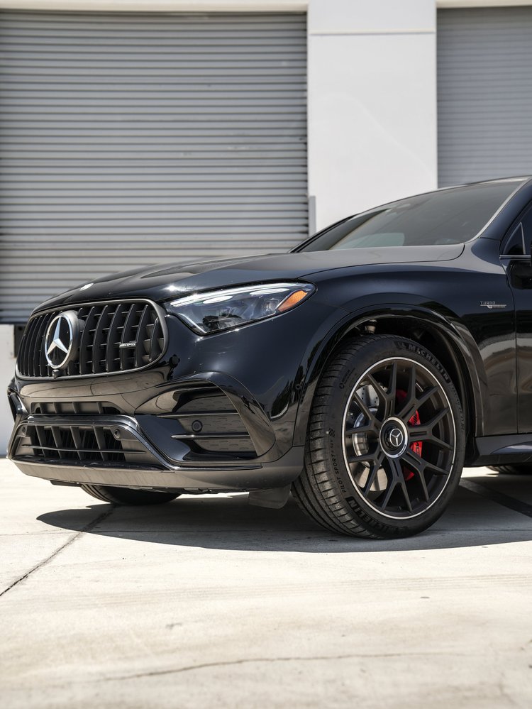 Low Mercedes-AMG GLC 63 S front-detail view showing the vertical-bar grille, Mercedes star, headlight, front wheel and red brake caliper.