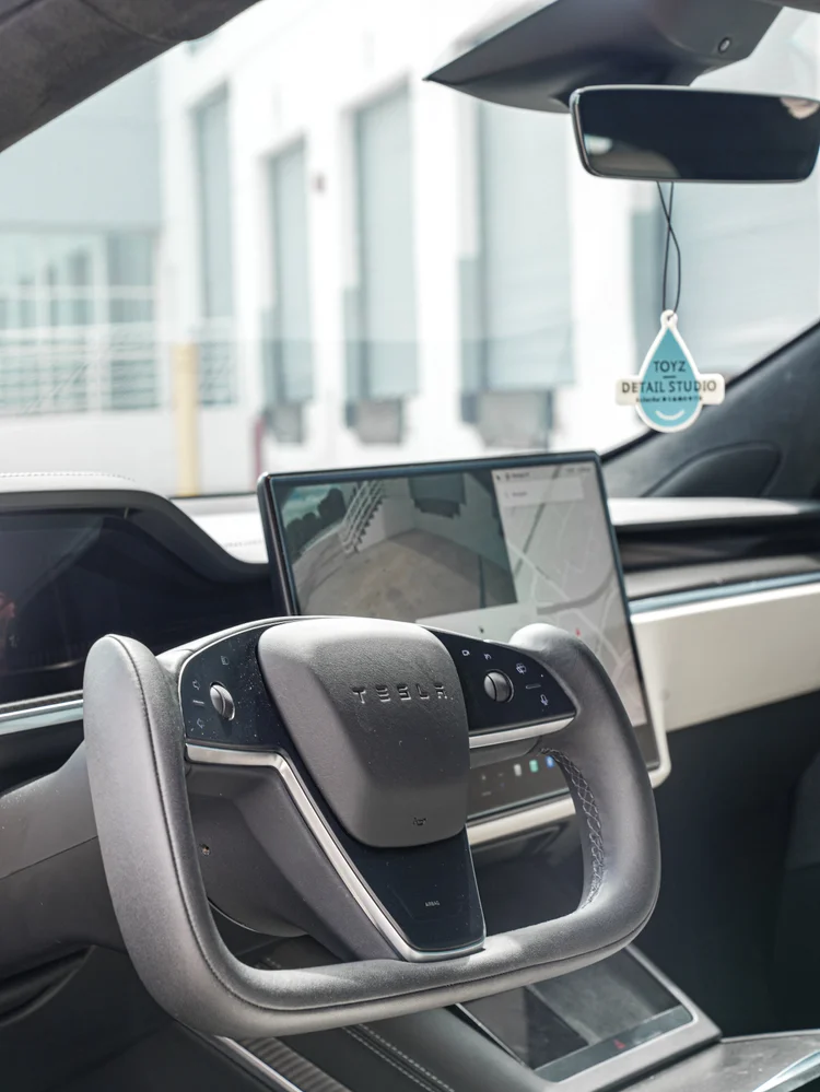 Tesla Model S cabin with a steering yoke, touchscreen, rear-view mirror and a Toyz Detail Studio hanging tag.