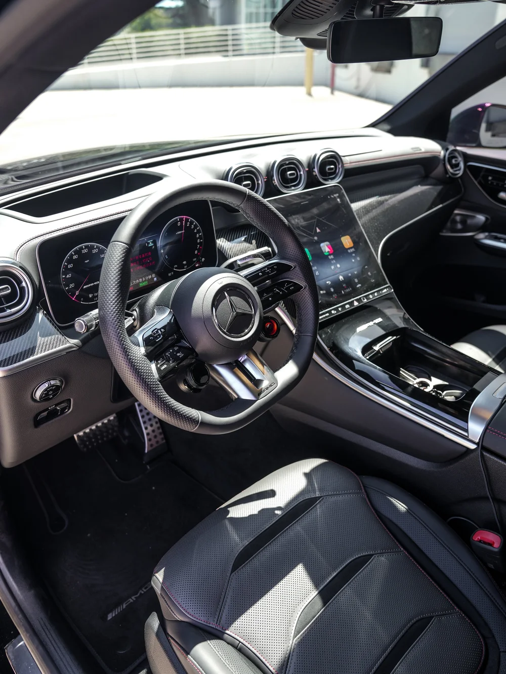 Mercedes-AMG GLC 63 S cockpit showing a Mercedes-star steering wheel, round air vents, a tall center display, woven-pattern trim and a dark perforated front seat.