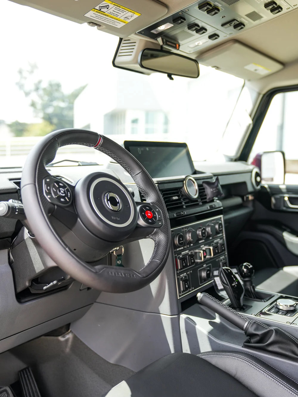 Driver cabin of the INEOS Grenadier with steering wheel, center controls and overhead switch panel.