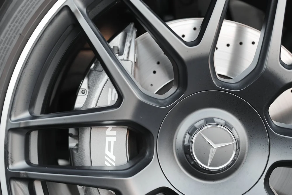 Close view through the G63 black wheel spokes to the grey AMG brake caliper, perforated disc and Mercedes center cap