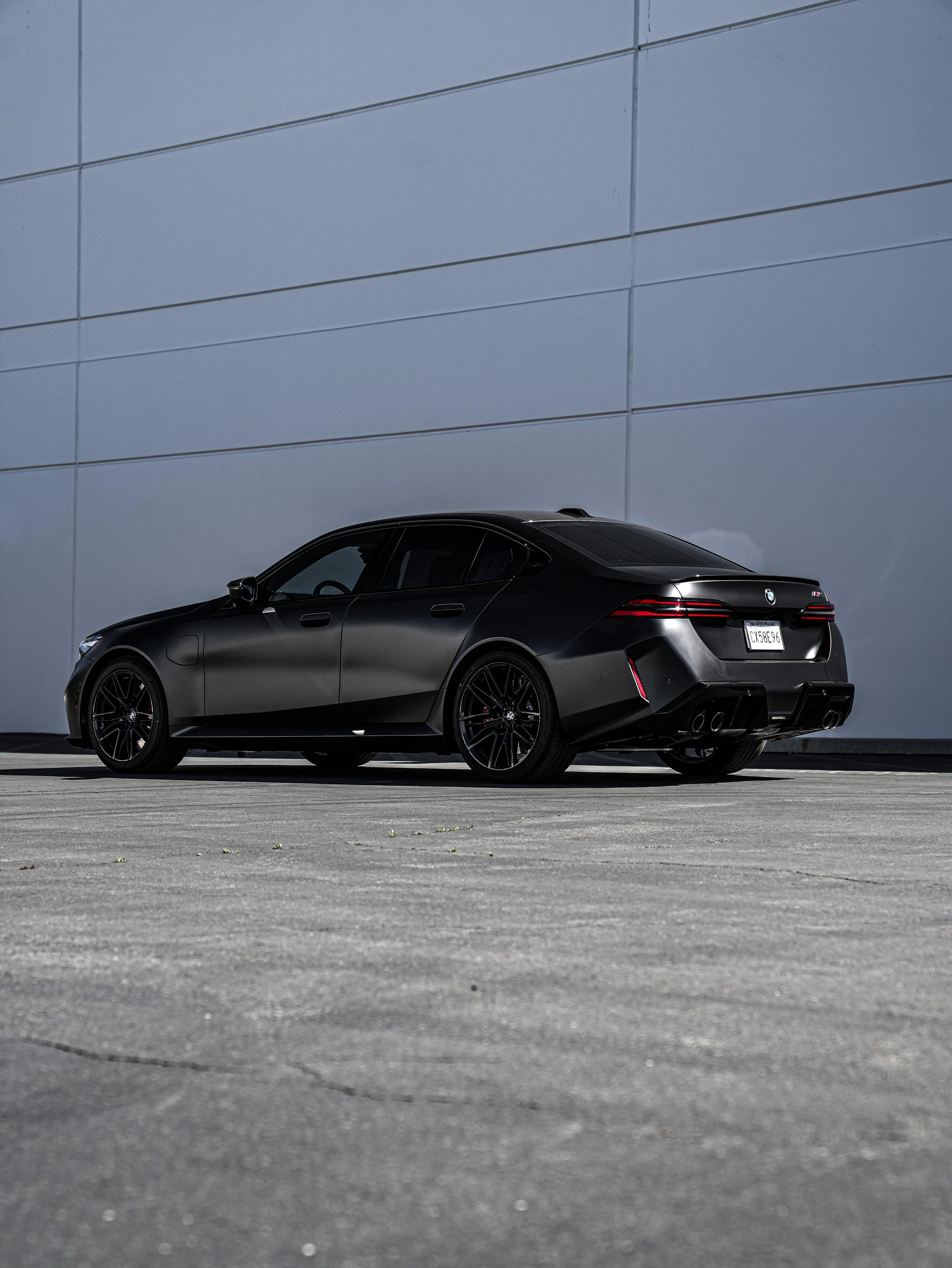 Black BMW M3 parked on a concrete surface against a plain, light-colored wall