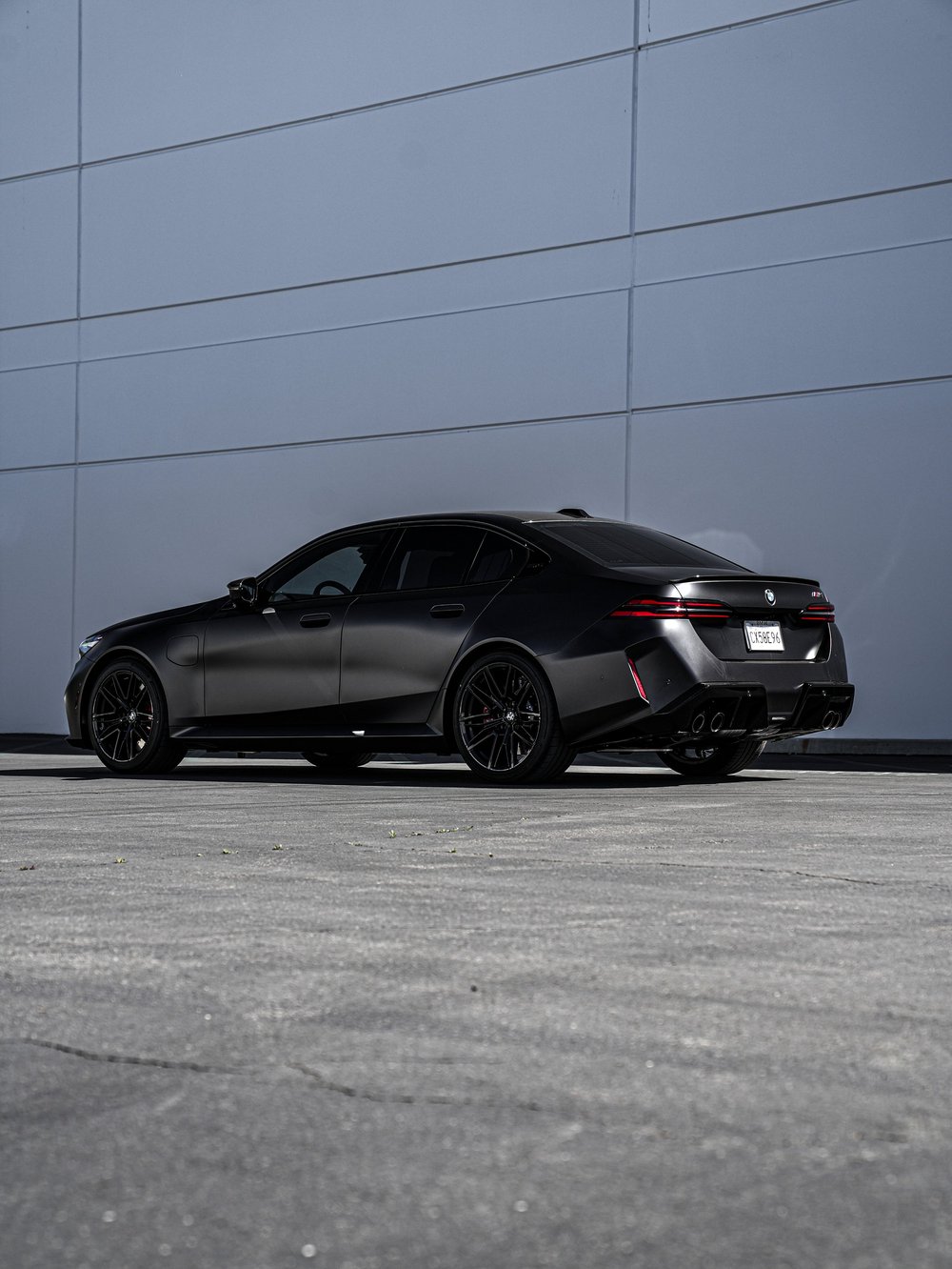 BMW G90 M5 in a full rear three-quarter view, showing matte side panels, black wheels and the rear bumper
