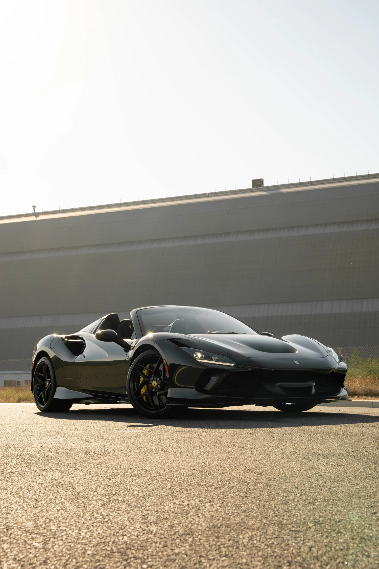 Low front three-quarter view of the black Ferrari F8 with open cockpit, black wheels and yellow brake calipers