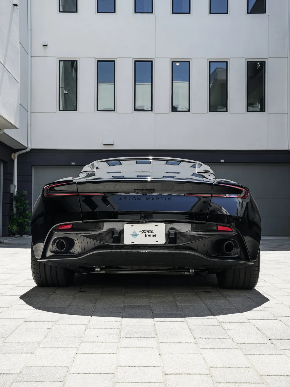 Complete rear view of the black DB12 with rear lamps, exhaust outlets and tires in a separate composition.