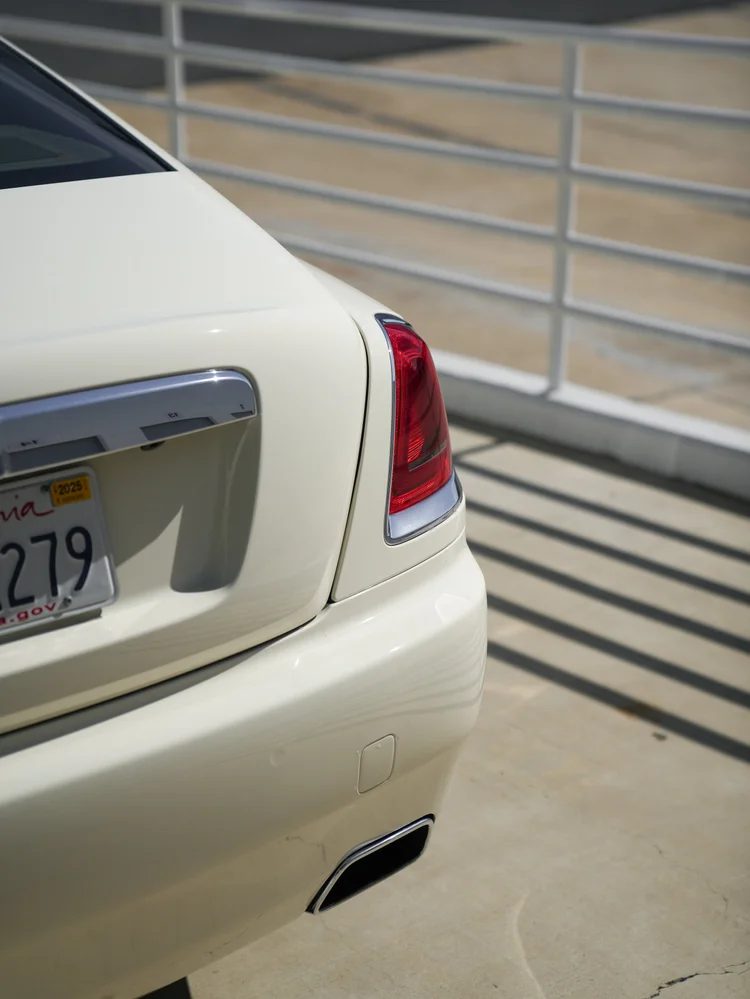 Pale Rolls-Royce Wraith rear corner with red taillamp, chrome trunk handle and exhaust opening.