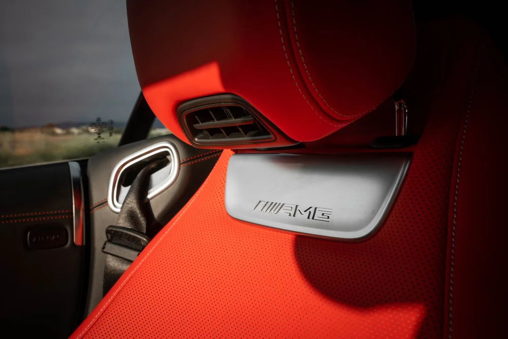 Red perforated seat detail with an AMG-lettered bright plaque and a small black vent below the stitched headrest