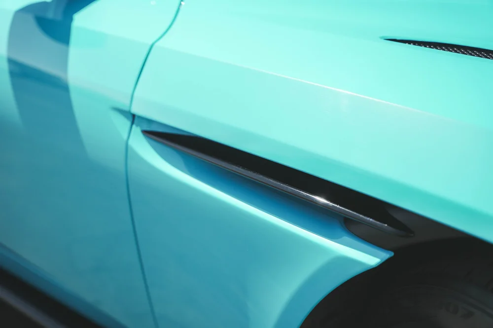 Black DB11 side vent recessed in Miami Blue front-fender contours beside the door seam