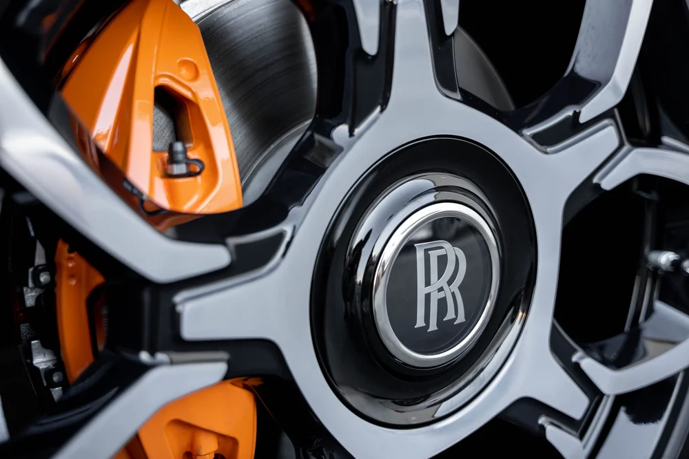 Black Rolls-Royce Cullinan Black Badge — bright wheel-spoke faces, RR center emblem and orange brake caliper
