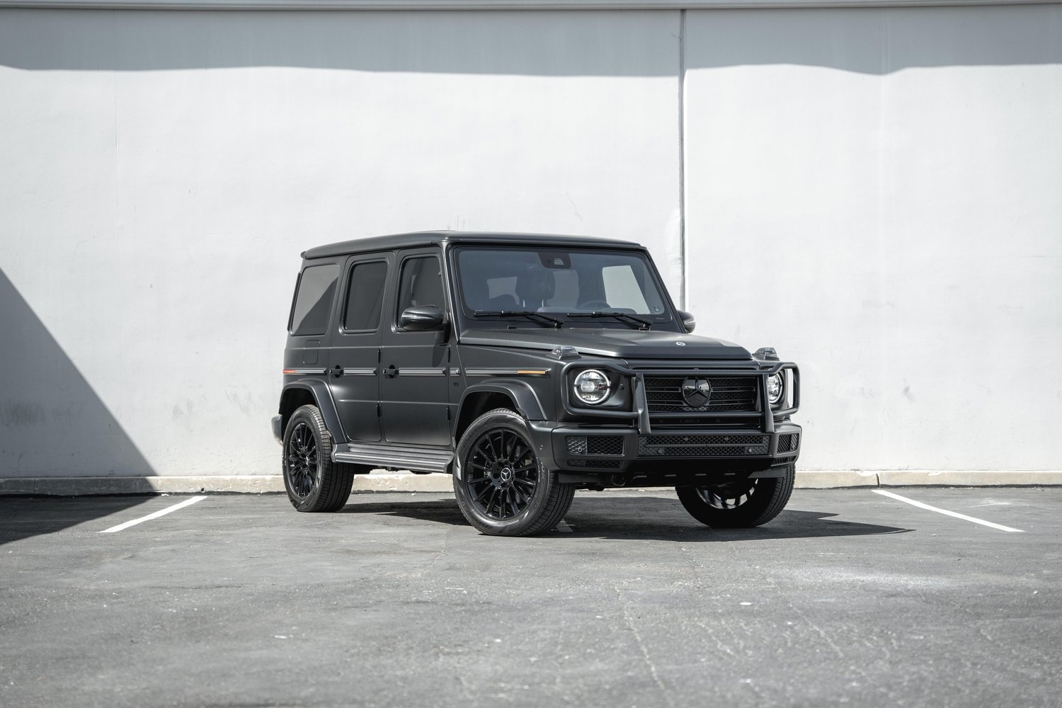 Landscape complete front-three-quarter view of the dark grey G 550 with black wheels, circular headlamps and a Mercedes-star grille