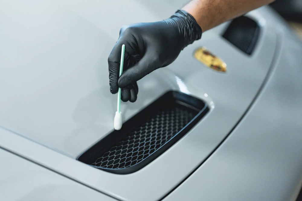 Technician carefully treating exterior plastic and trim on a Porsche.