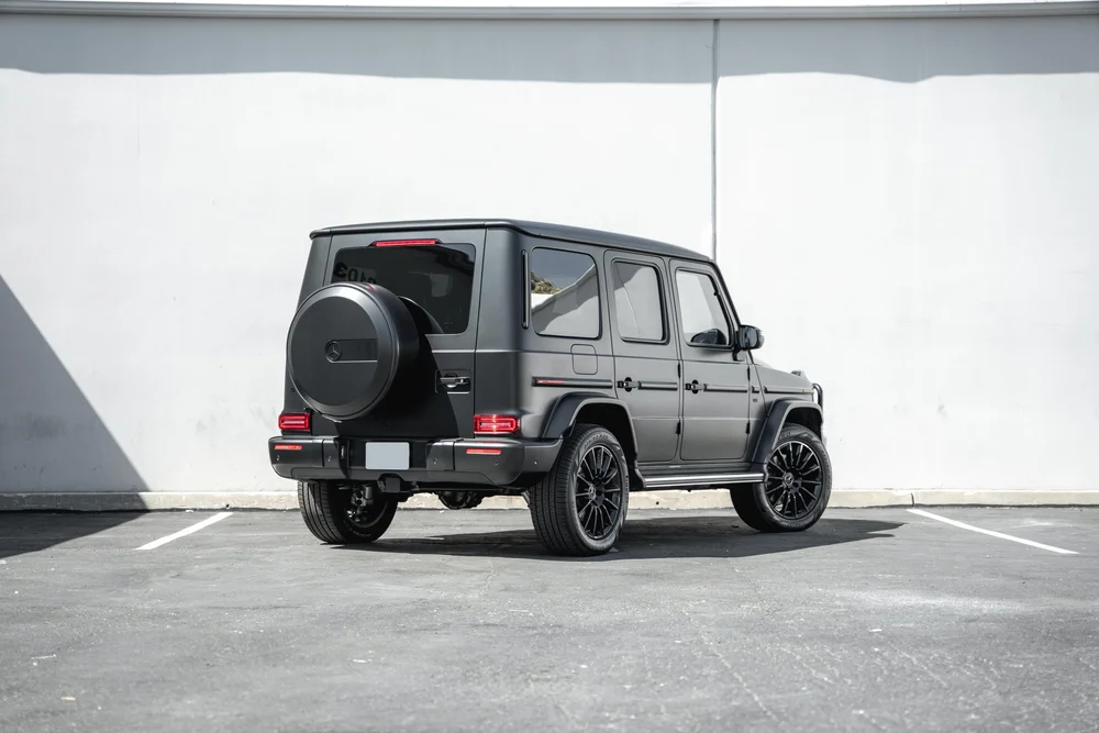 Complete rear-three-quarter view of the dark grey Mercedes-Benz G 550 with black wheels, red rear lamps and a round spare-wheel cover