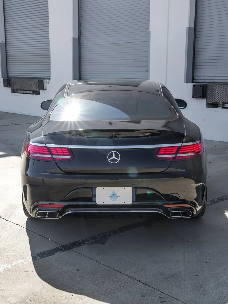 Straight rear view of the black Mercedes-Benz S 560 coupe showing segmented red taillights, a Mercedes star, bright trunk trim and paired rectangular exhaust outlets.