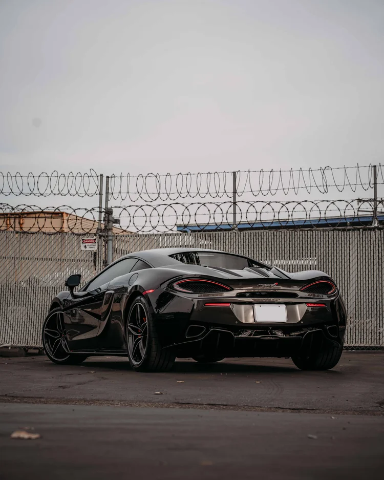 Complete rear-three-quarter portrait of the dark coupe with red lamp outlines and silver-edged wheels.