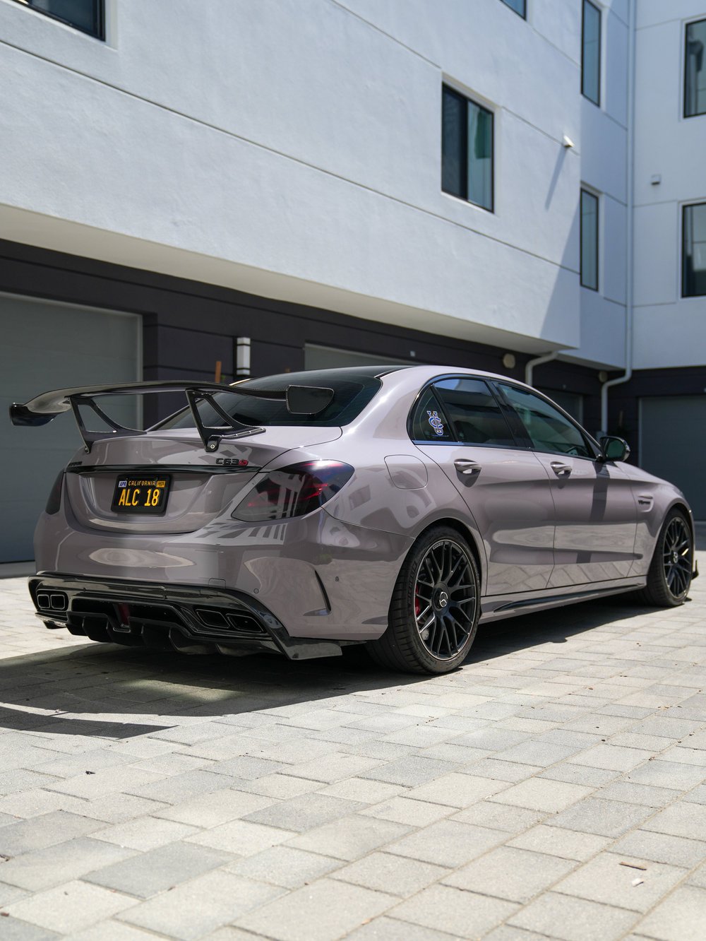 Complete rear three-quarter view of the light-grey C 63 S with a tall wing, dark wheels and four exhaust outlets