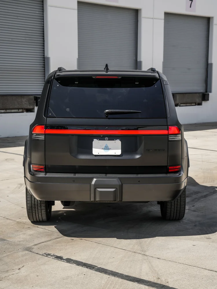 Complete straight rear view of the dark GX 550 with a red full-width light bar, LEXUS lettering, rear wiper and GX550 badge outside garage doors