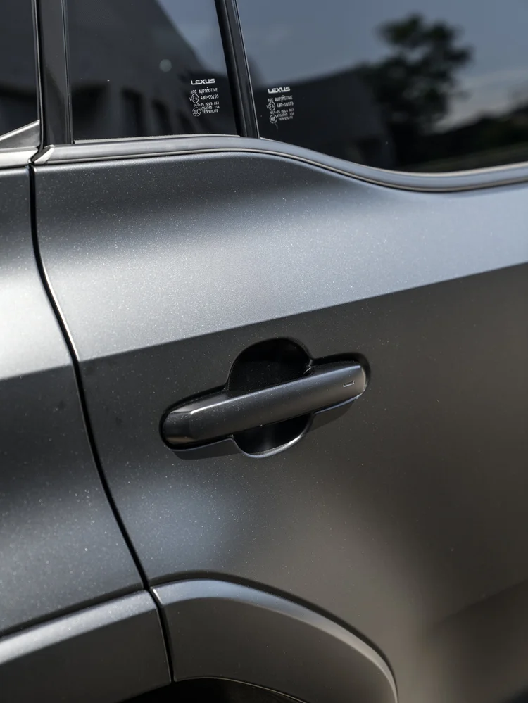 Dark door handle and sculpted upper door contour below reflective side glass bearing small LEXUS lettering
