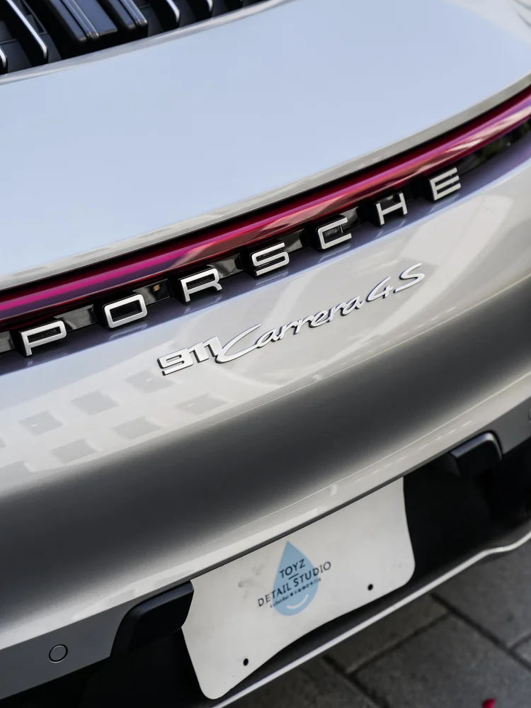 Tilted close rear view of the silver Porsche 911 showing the red lamp strip, Porsche lettering, visible 911 Carrera 4 S badge and white Toyz plate.