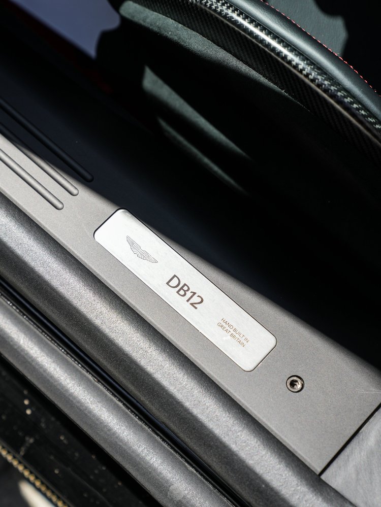 DB12 door-sill plaque with the Aston Martin emblem beside dark interior trim.