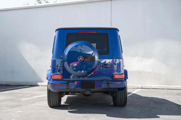 Complete straight rear view of the blue G 63 with red lamps and reflections across its round spare-wheel cover