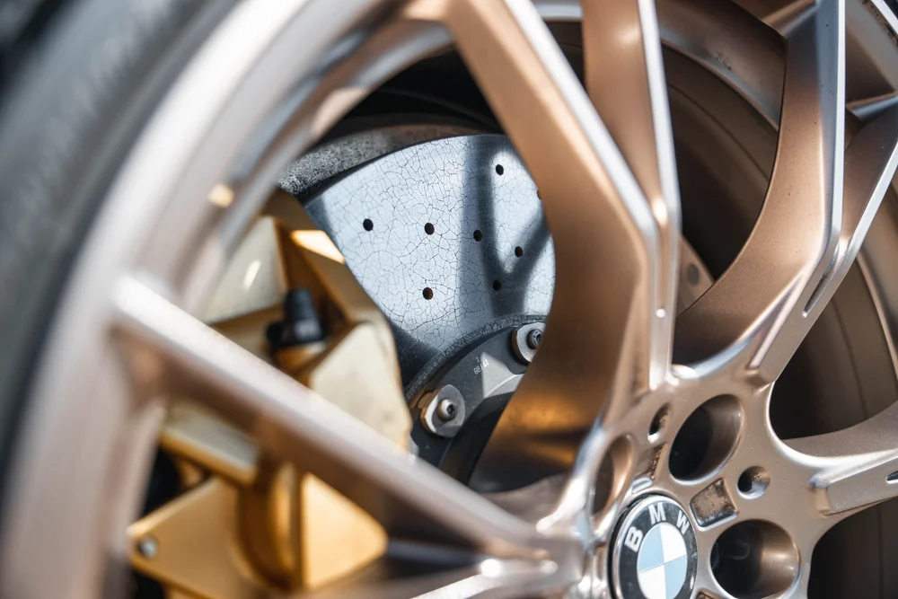 Close view through bronze-colored BMW M5 CS wheel spokes to a drilled brake disc, gold-colored caliper and BMW center emblem