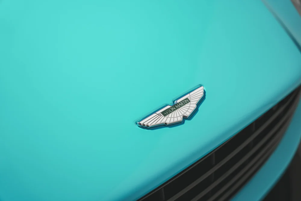 Winged Aston Martin badge on the Miami Blue DB11 hood above the black grille edge