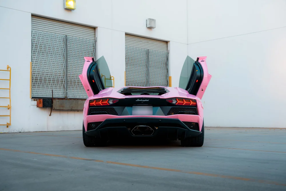 Sakura Pink Lamborghini Aventador seen directly from the rear with both scissor doors raised