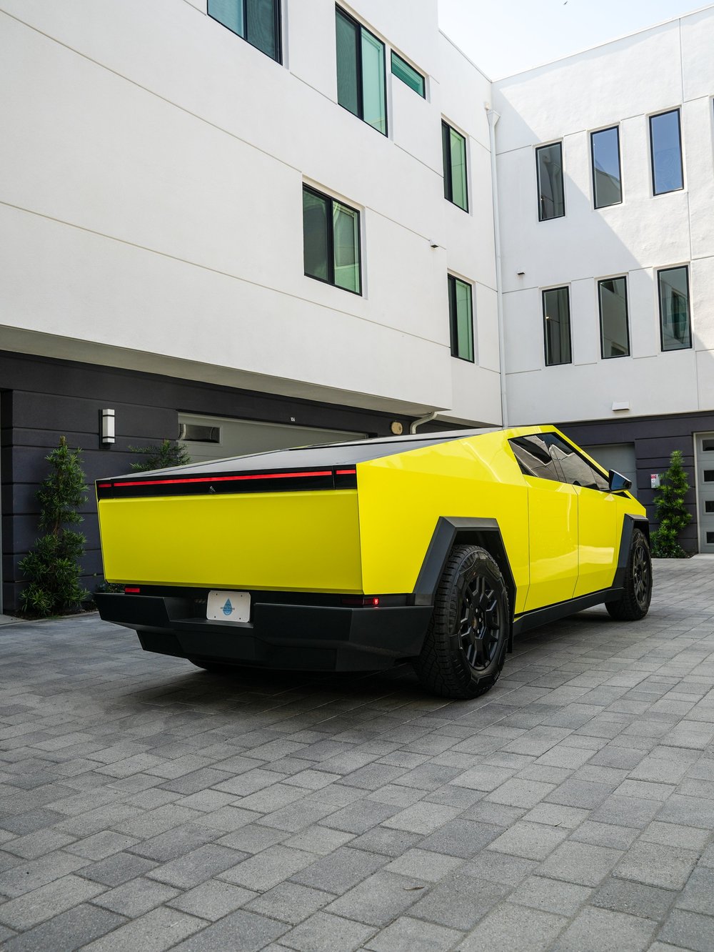 Complete right-facing rear three-quarter view of the Racing Yellow Tesla Cybertruck showing its yellow tailgate and side panels, red light bar, black wheels and rear bumper.
