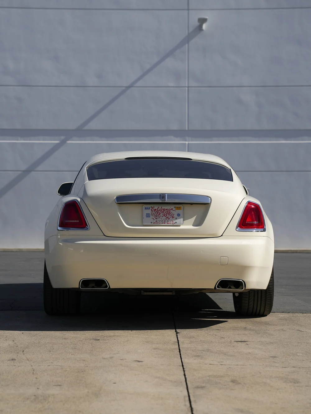 Straight-rear view of the pale Rolls-Royce Wraith with both taillamps, rear tires and exhaust openings.