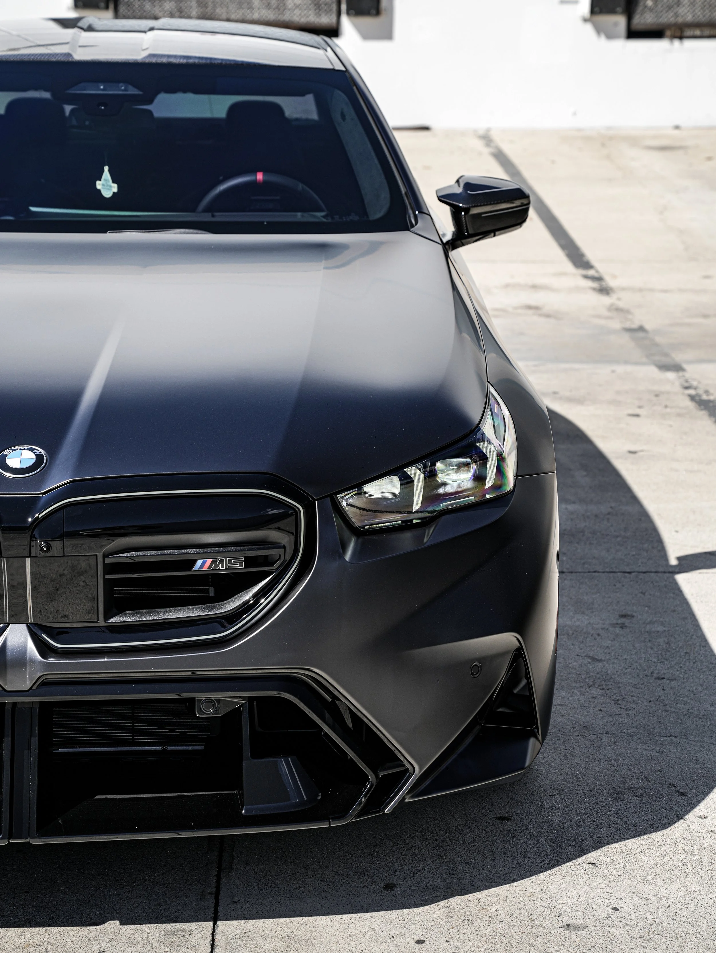 Close-up of the front of a black BMW M8 sports car parked on a concrete surface.