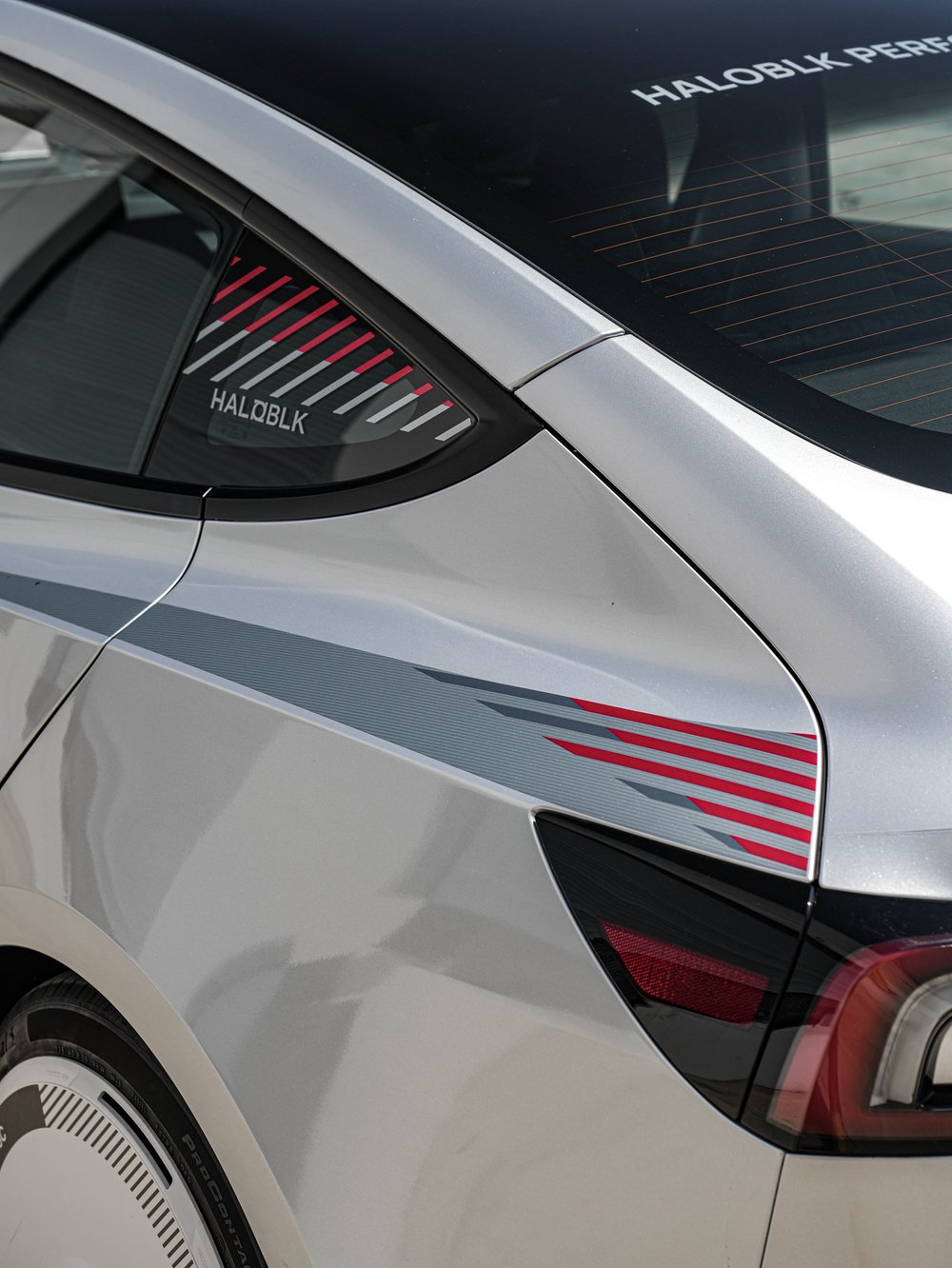HALOBLK lettering and red and white directional graphics on the Model 3 rear side glass above silver rear-quarter stripes and a tail light.