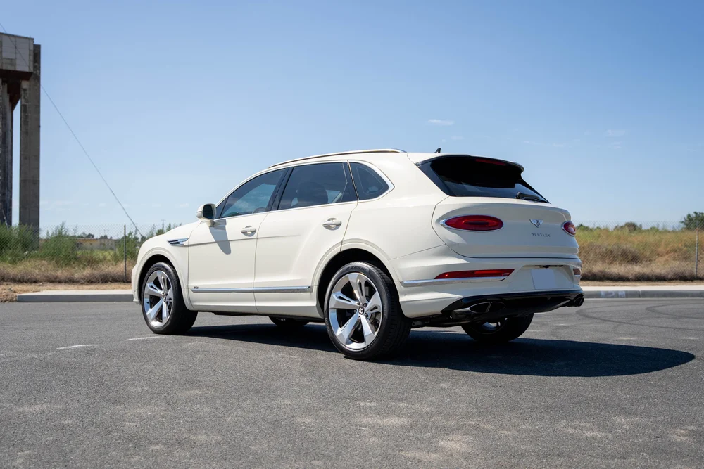 White Bentley viewed from the opposite rear corner beneath a clear sky.