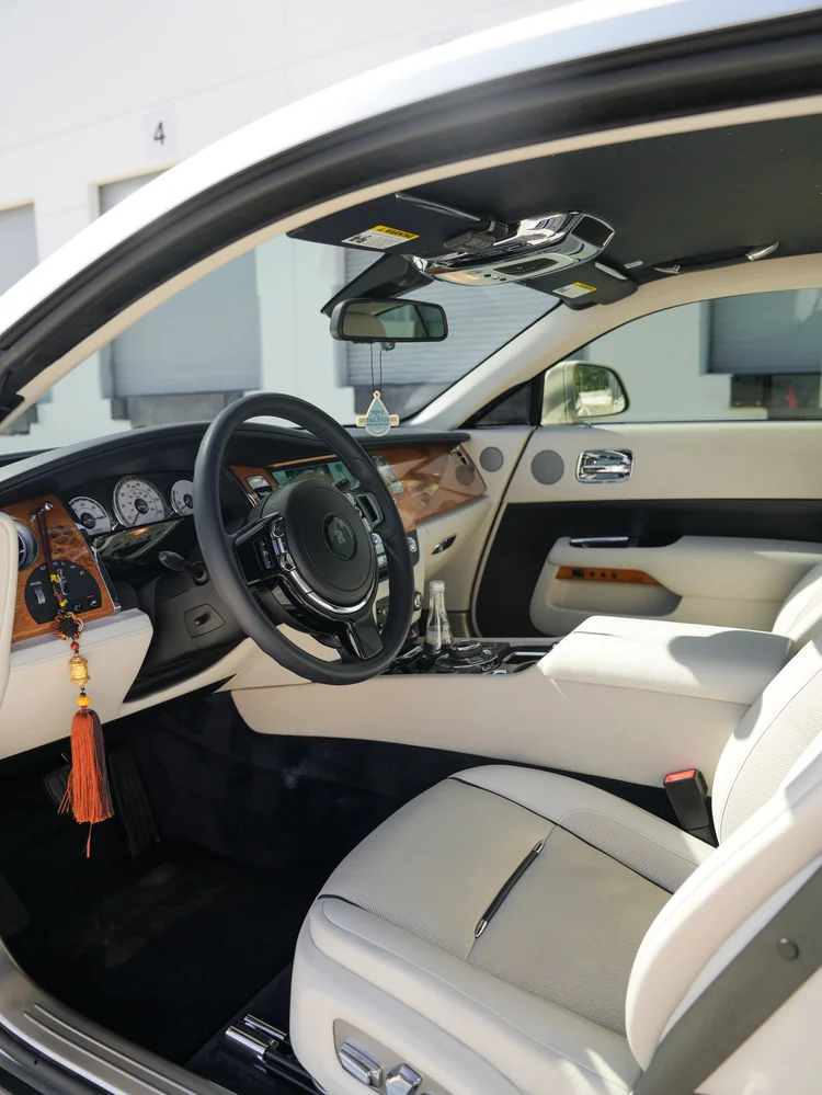 Rolls-Royce Wraith cockpit with steering wheel, analog instruments, wood dashboard and light front seat.