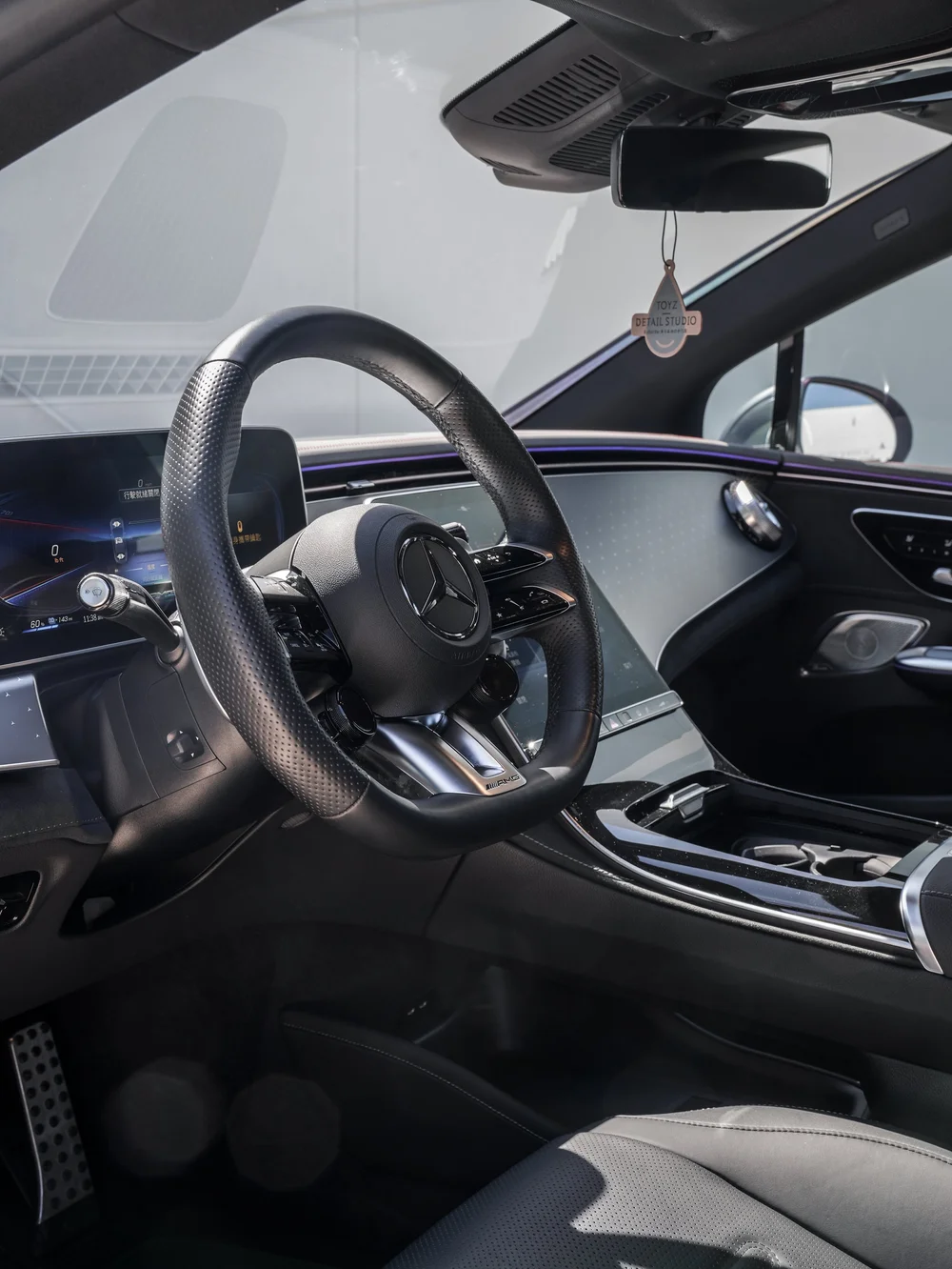 Driver cabin of the Mercedes-AMG EQE 53 with AMG steering wheel, display panel, center console and purple ambient lighting.