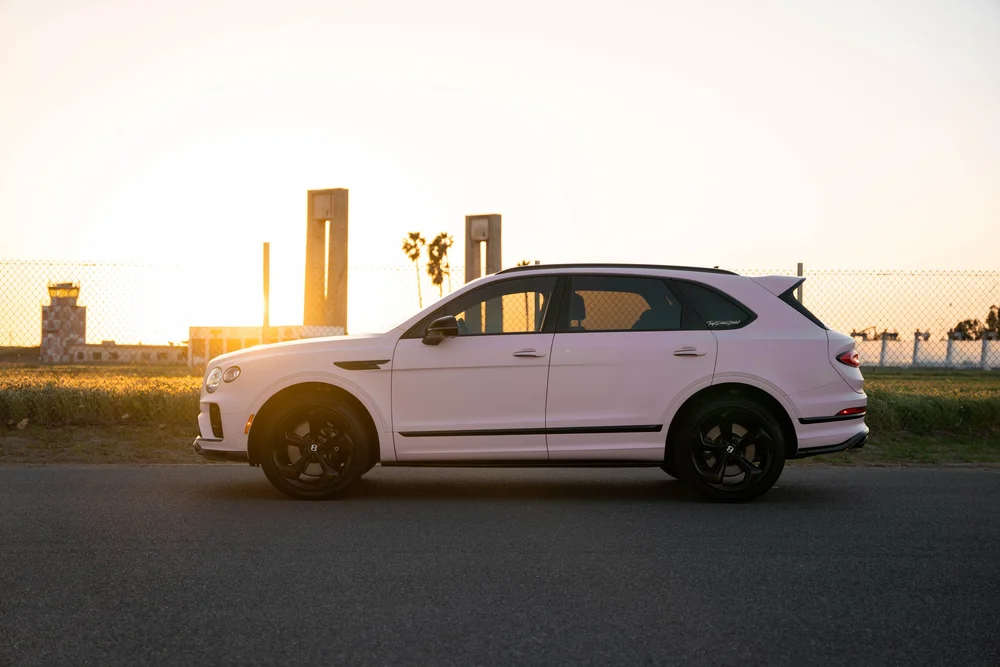 Full side profile of the Sakura Pink Bentayga with black wheels, dark glass and sunlight behind the front fender